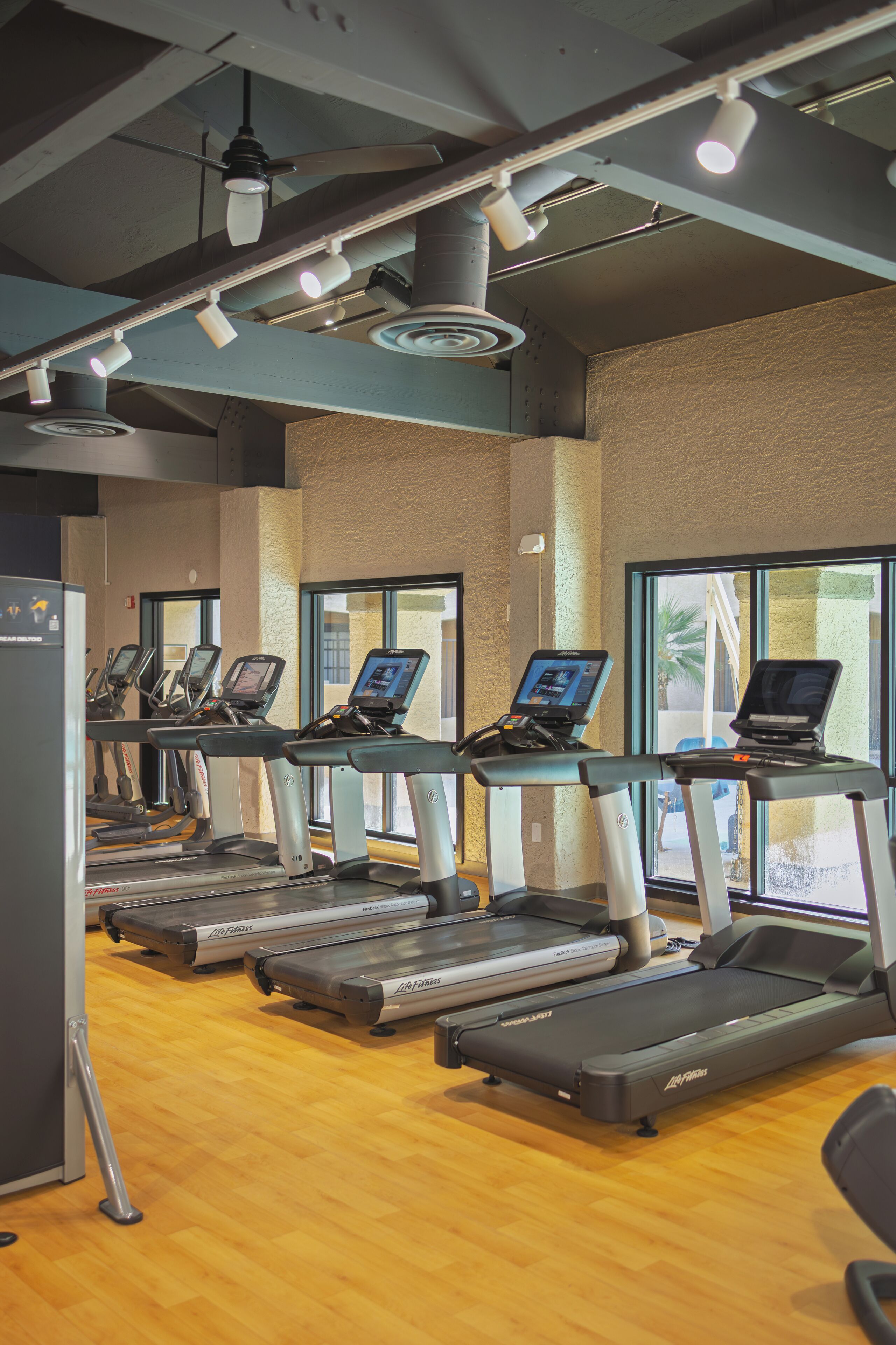 A gym with treadmills, exercise bikes, and a wooden floor.