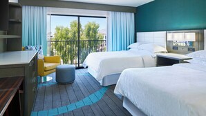 A hotel room with two beds, a desk, a chair, and a balcony with a view of trees and buildings. - Sheraton Tucson Hotel and Suites (Tucson)
