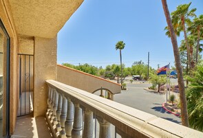 A balcony with a view of a street, palm trees, and a flag.