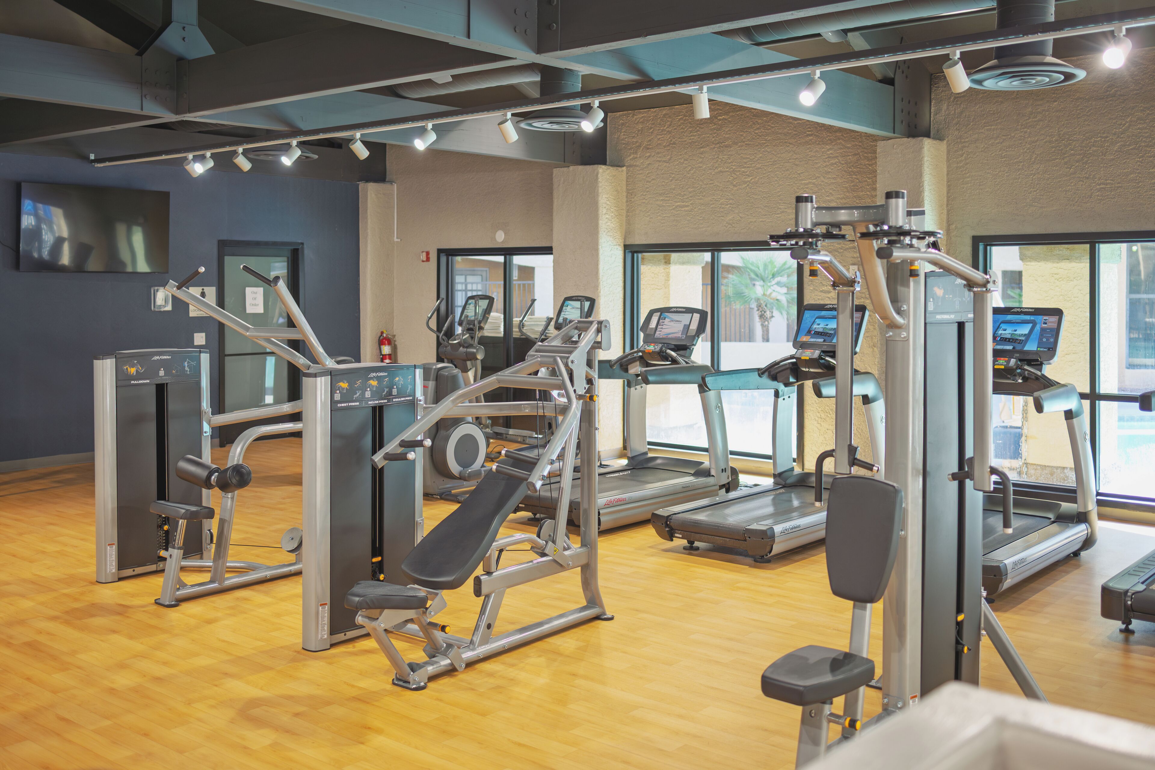 A gym with exercise equipment, a wooden floor, and large windows.