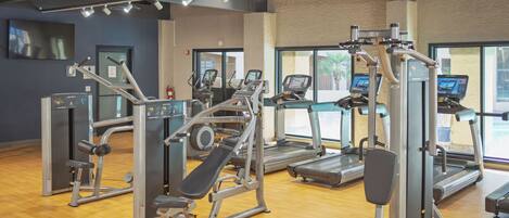 A gym with exercise equipment, a wooden floor, and large windows.