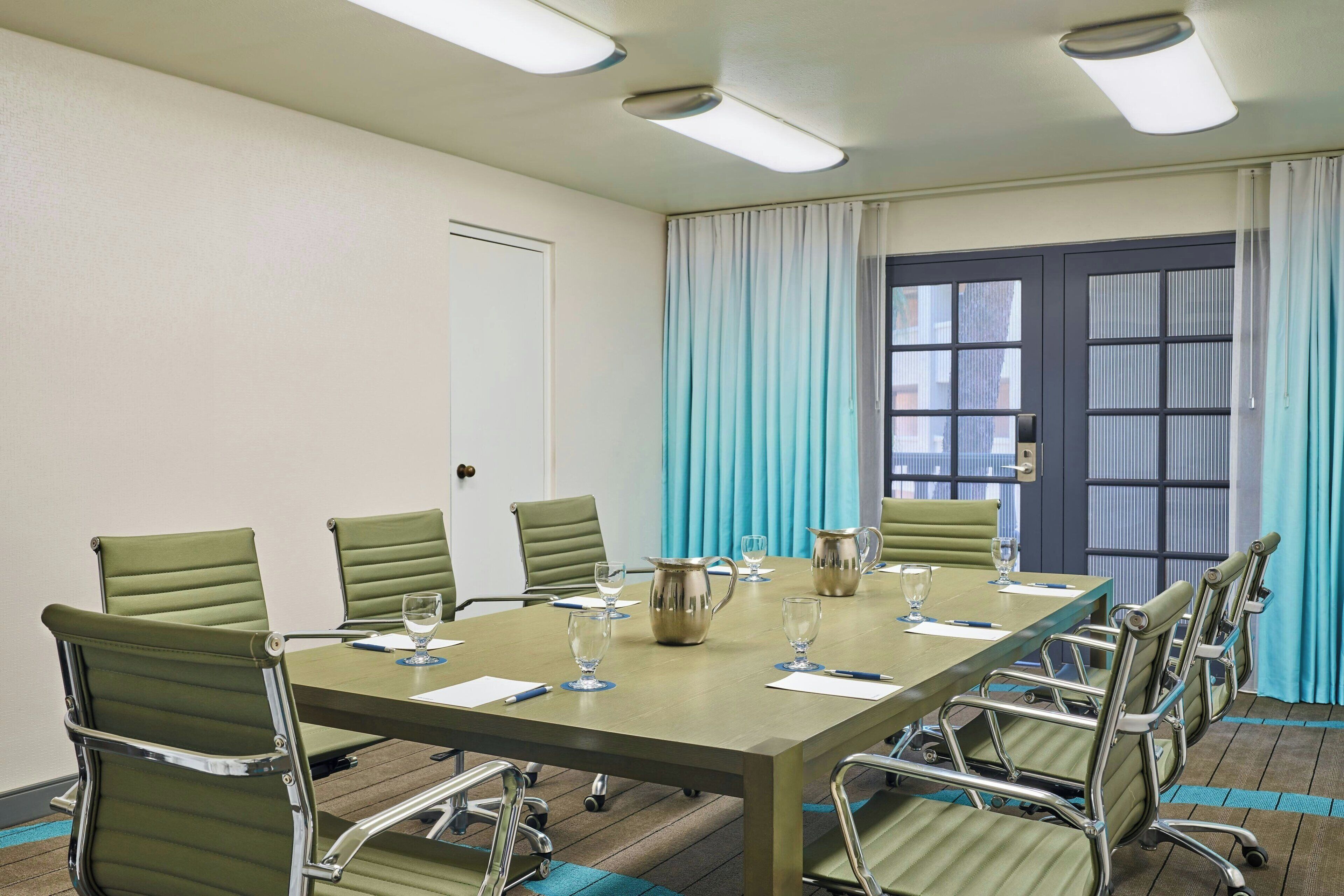A conference room with a long table, six chairs, and a pitcher of water.