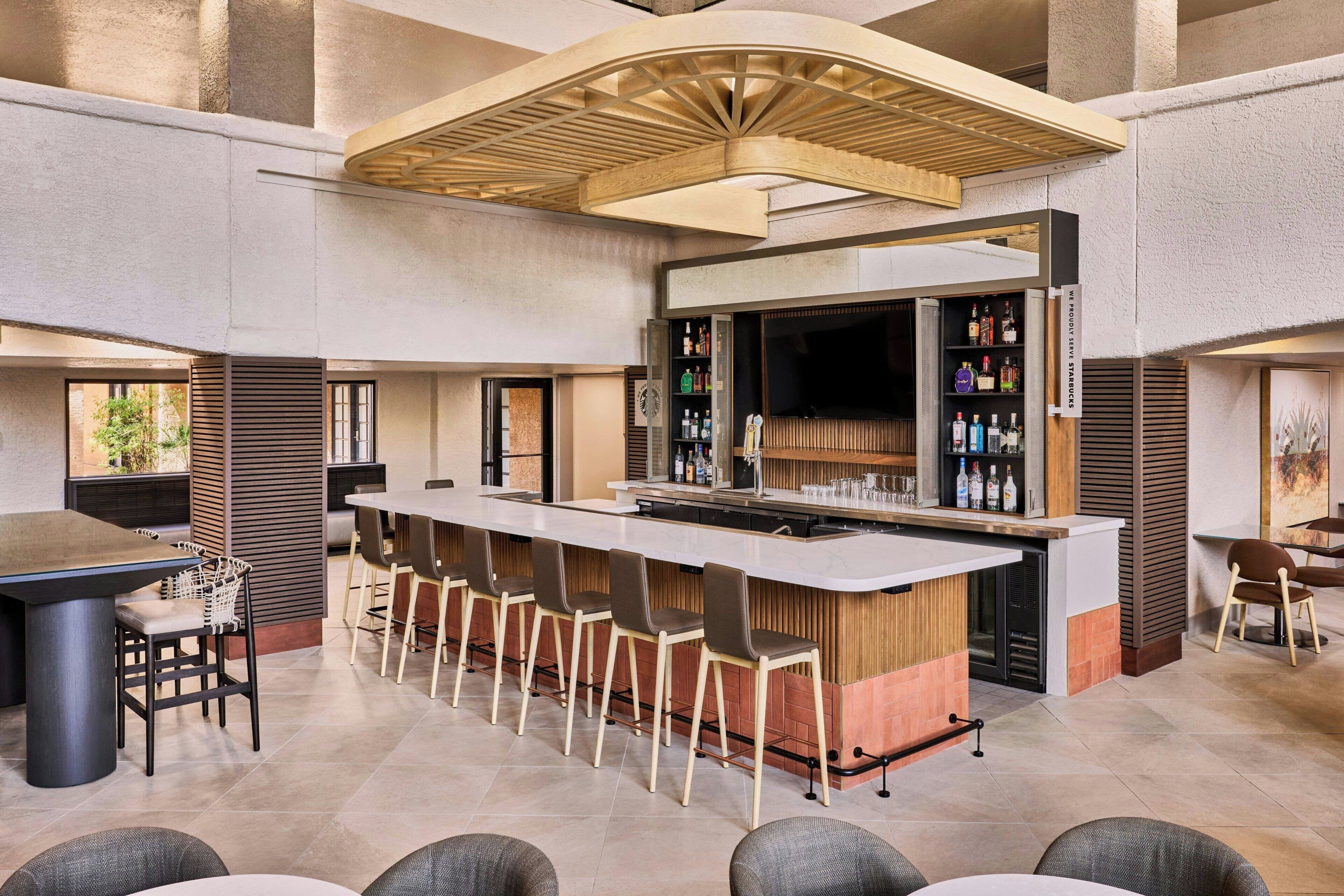 A modern bar area with a long counter, bar stools, and a variety of liquor bottles.