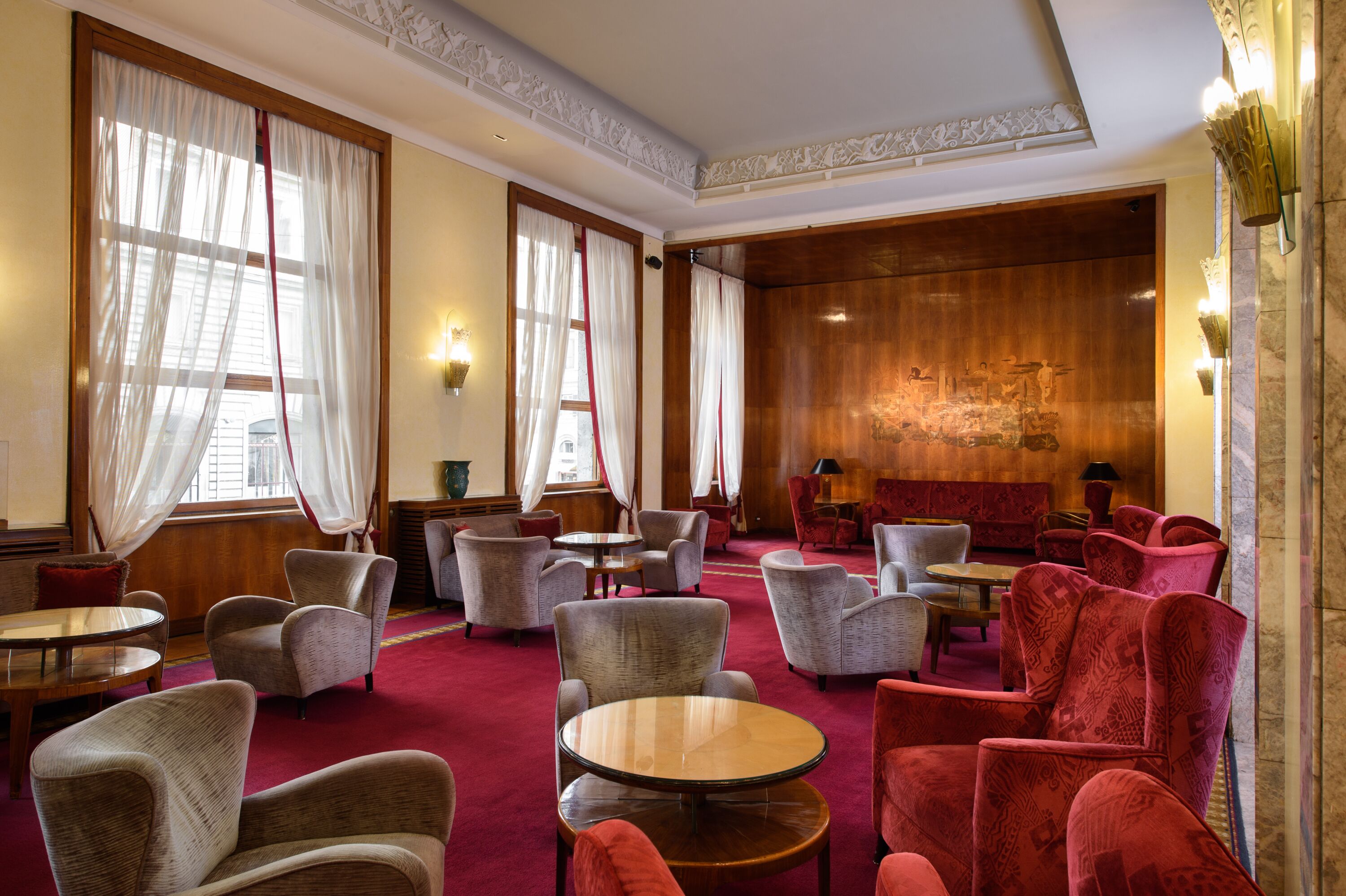 A hotel lobby with multiple seating areas, including round tables and chairs, and a red sofa.