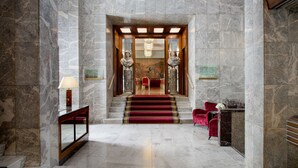 Un vestíbulo con suelo de mármol y una escalera con alfombra roja, una recepción y una silla roja.