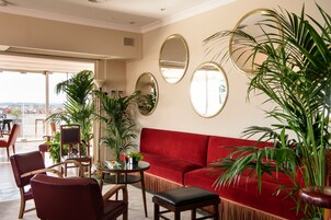 A red sofa, multiple chairs, a small table, and several potted plants in a well-lit room with large mirrors on the wall.
