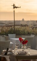 A dining table set with wine glasses and a bottle, overlooking a cityscape with a prominent dome structure.