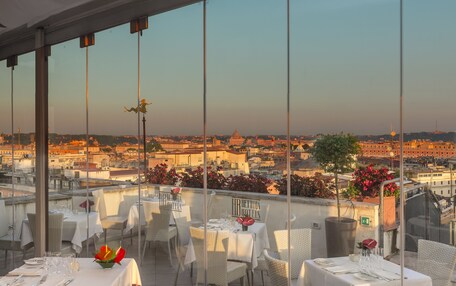 A rooftop restaurant with tables set for dining, overlooking a cityscape.