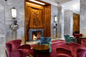 A lobby with a fireplace, marble walls, and red upholstered chairs.