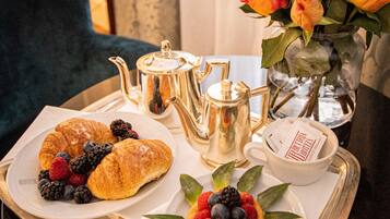 A tray with croissants, berries, a small fruit tart, a teapot, a cup, and a vase of flowers.