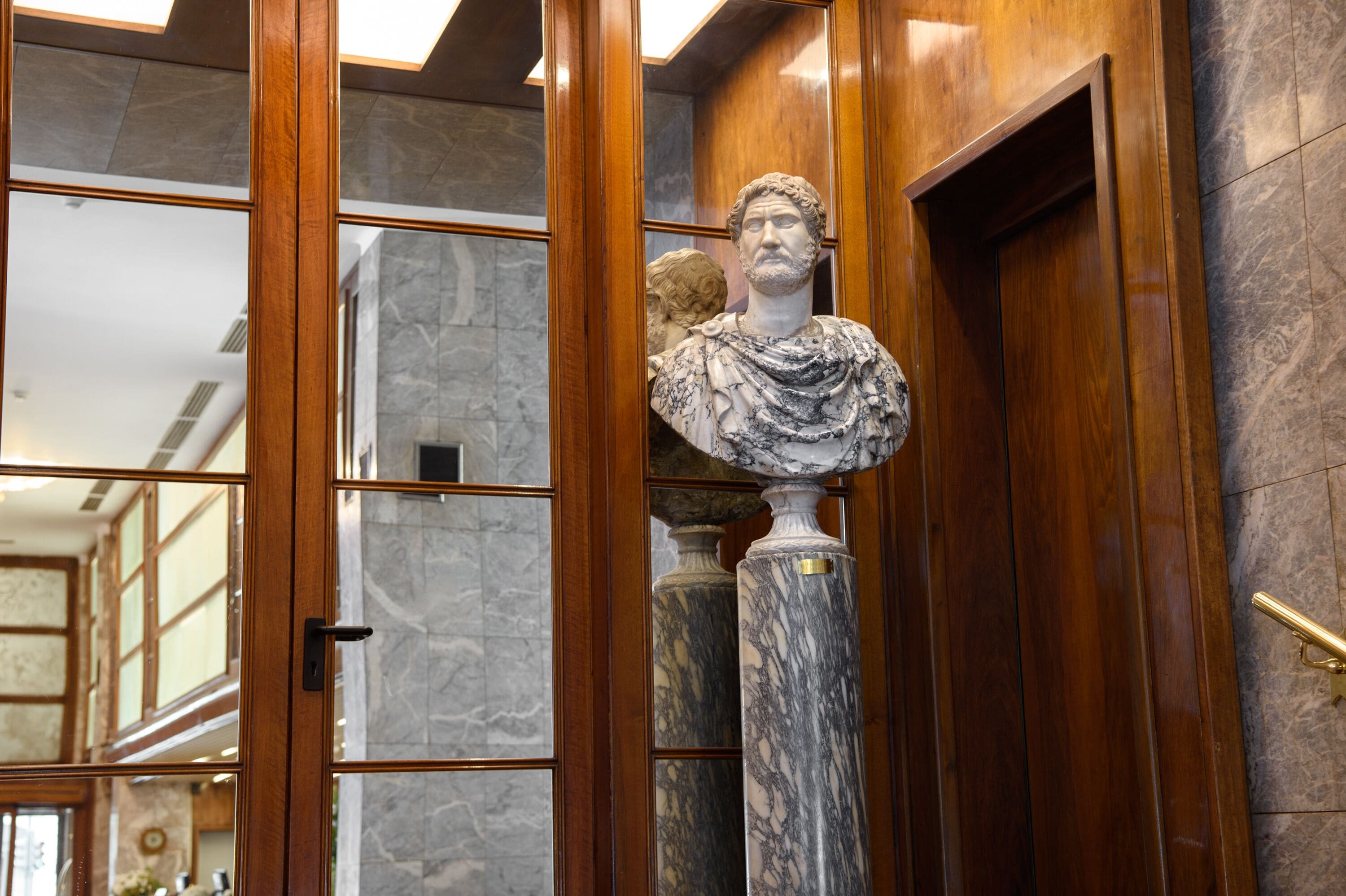 A marble bust on a column in a lobby with wooden paneling and marble flooring.