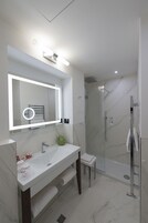 A modern bathroom with a large mirror, a white sink, a glass-enclosed shower, and marble flooring.