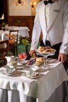 A table set for a meal with a teapot, cups, a bowl of fruit, and a cake stand with pastries.