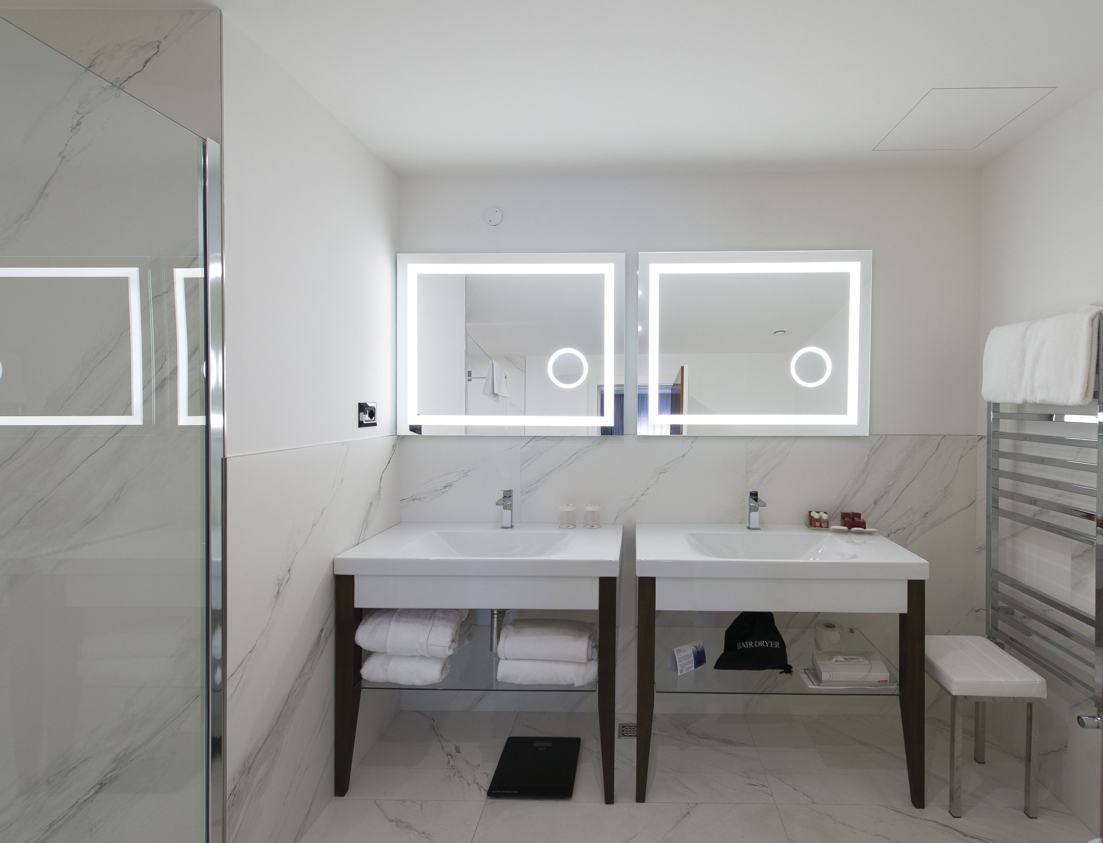 A modern bathroom with two sinks, a glass shower enclosure, and a towel rack.