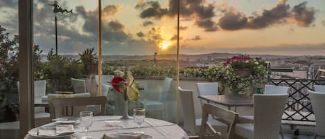 A table set for dining with a view of the sunset over a cityscape.