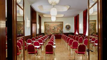 Une salle de conférence avec des rangées de chaises rouges, un plancher en bois et un grand tableau accroché au mur.