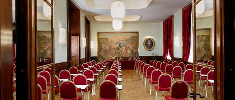 A conference room with rows of red chairs, a wooden floor, and a large painting on the wall.