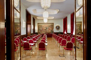 A conference room with rows of red chairs, a wooden floor, and a large painting on the wall.