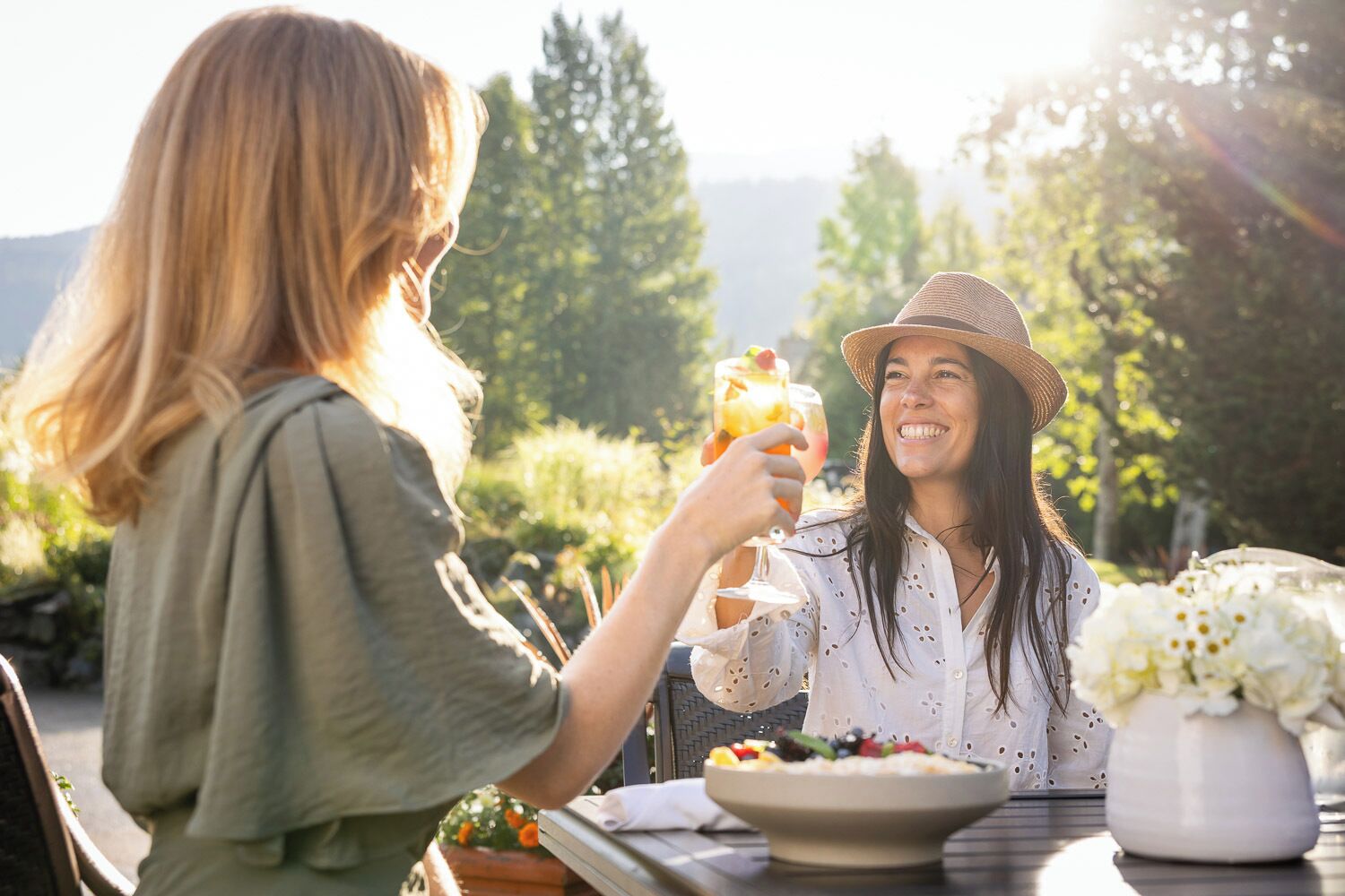 Two people sitting at an outdoor table with a bowl of fruit and a glass of drink.