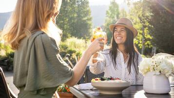 Deux personnes sont assises à une table en plein air, devant un saladier rempli de fruits et un verre contenant une boisson.