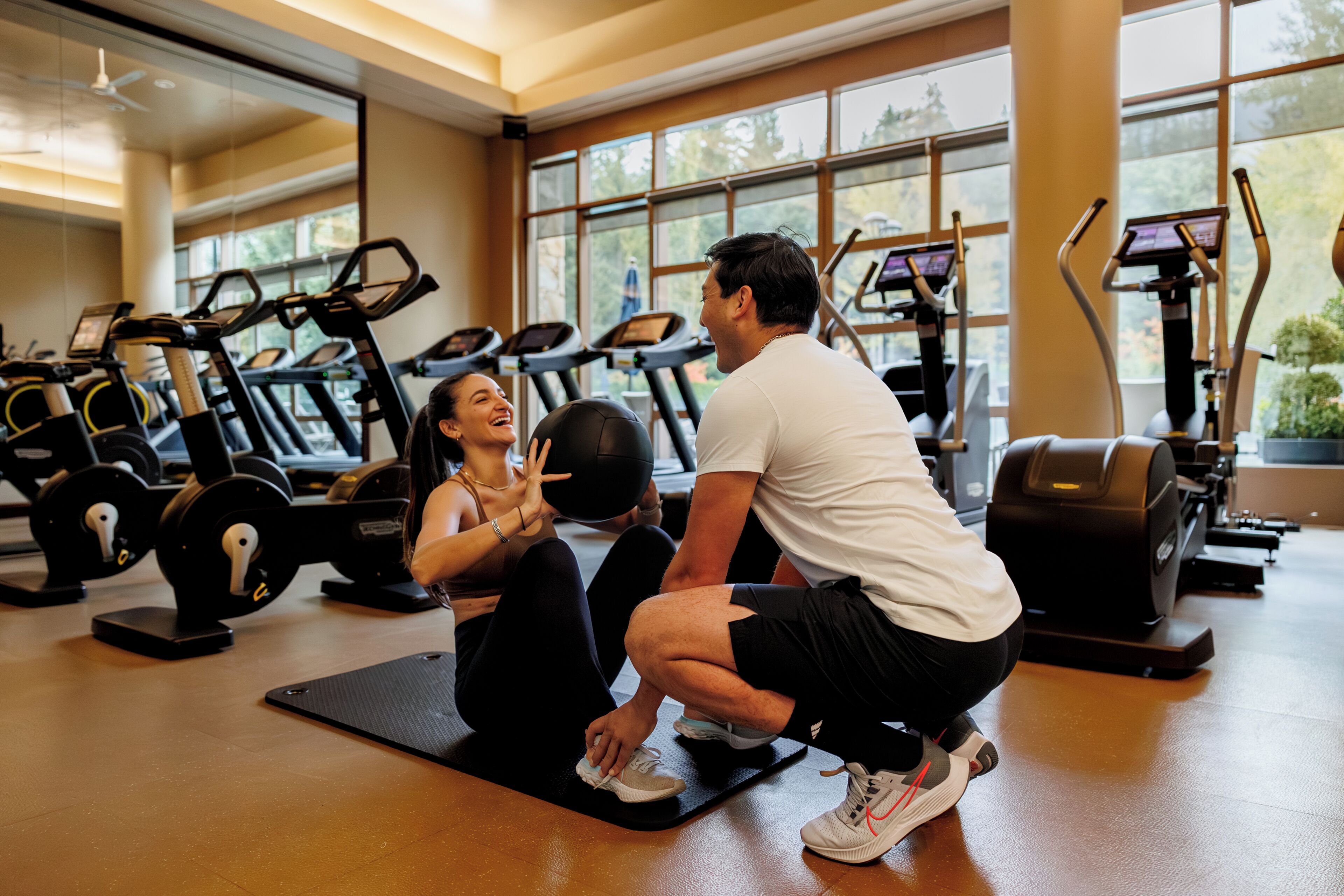 Ein Fitnessraum mit Trainingsgeräten, großen Fenstern und Holzboden.
