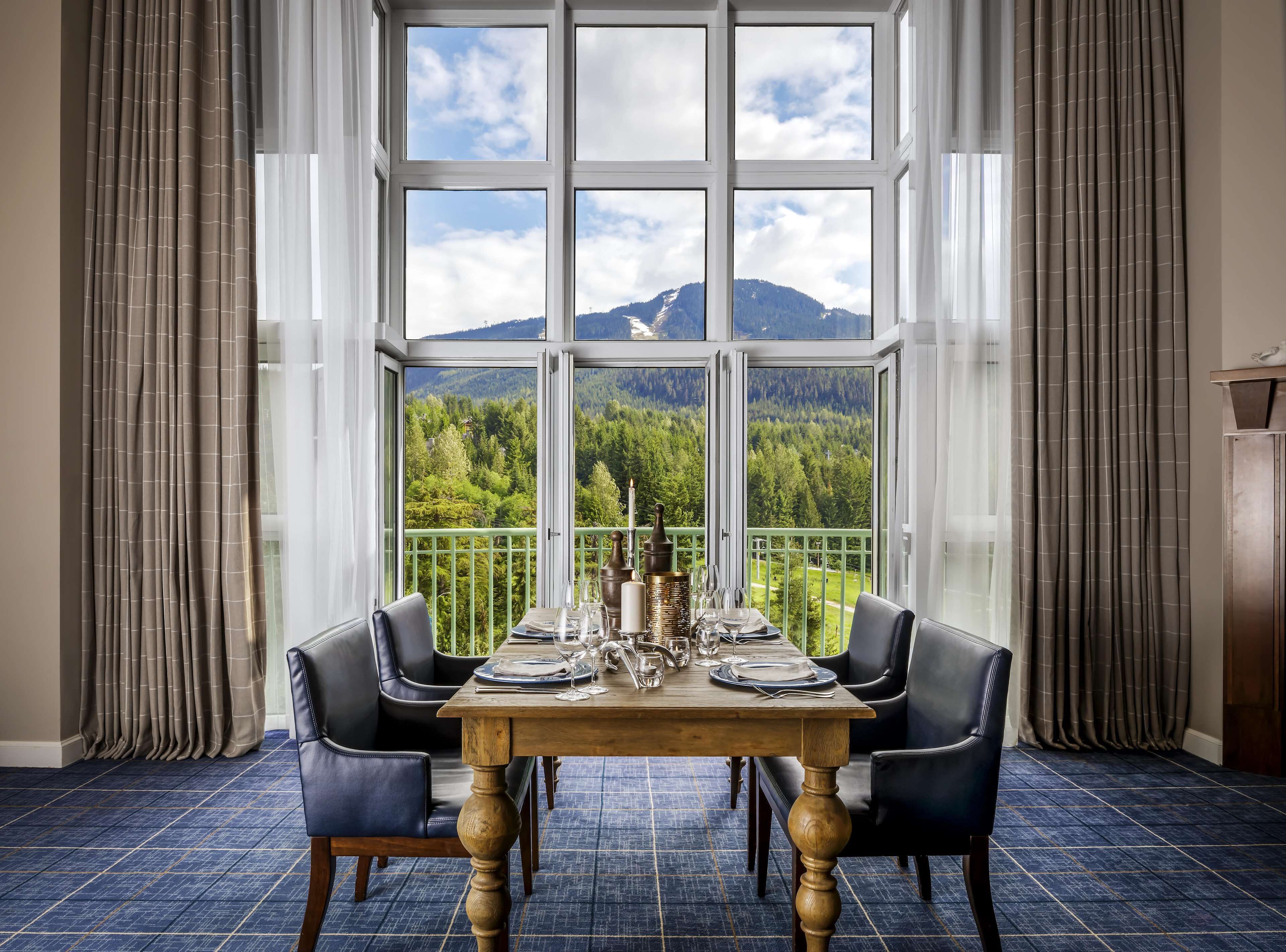 A dining area with a table set for four, large windows, and a view of a mountainous landscape.