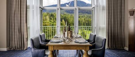 A dining area with a table set for four, large windows, and a view of a mountainous landscape.