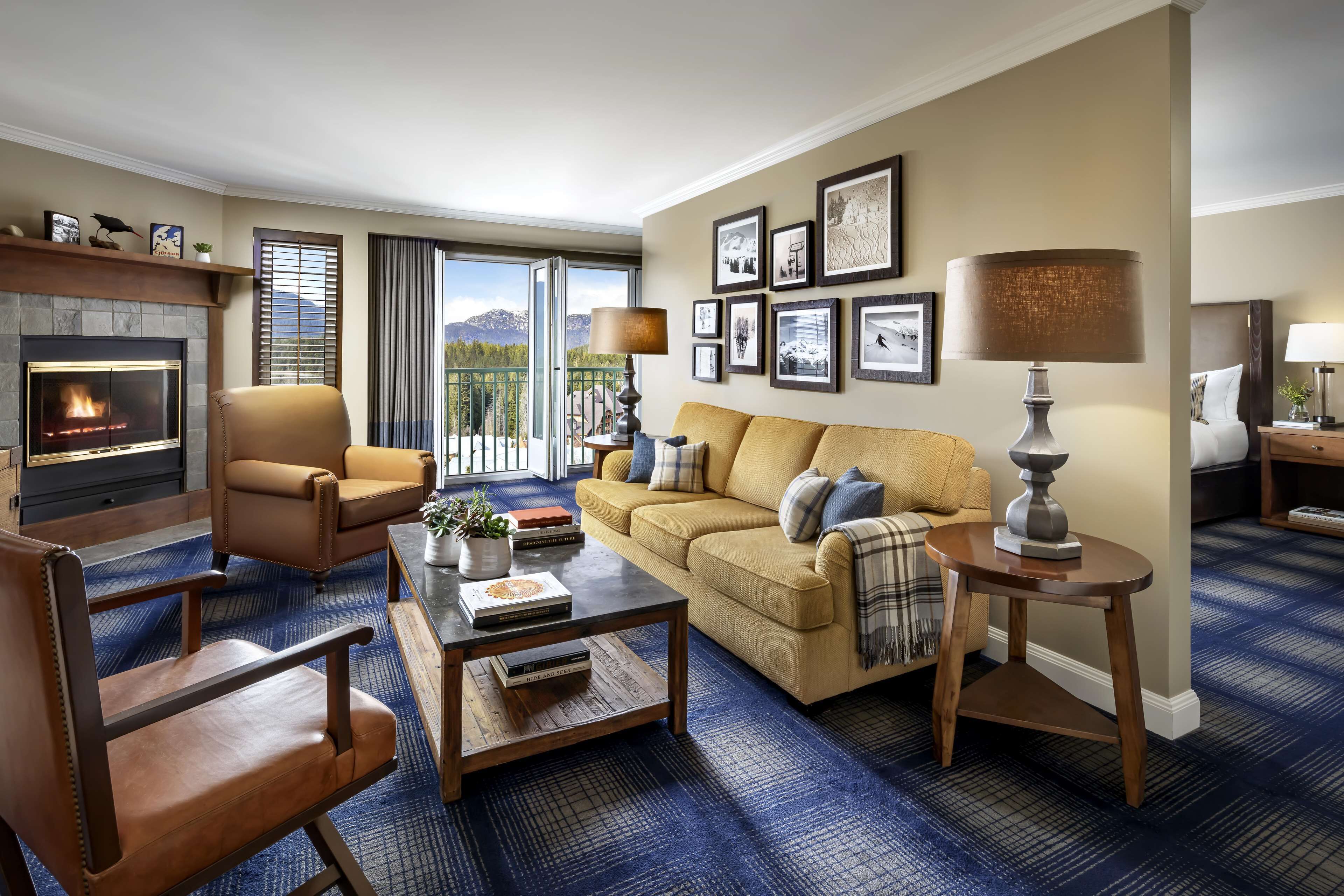 A living room with a fireplace, a sofa, a coffee table, and a view of mountains through large windows.
