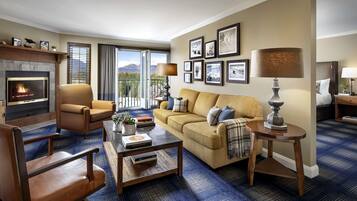 A living room with a fireplace, a sofa, a coffee table, and a view of mountains through large windows.