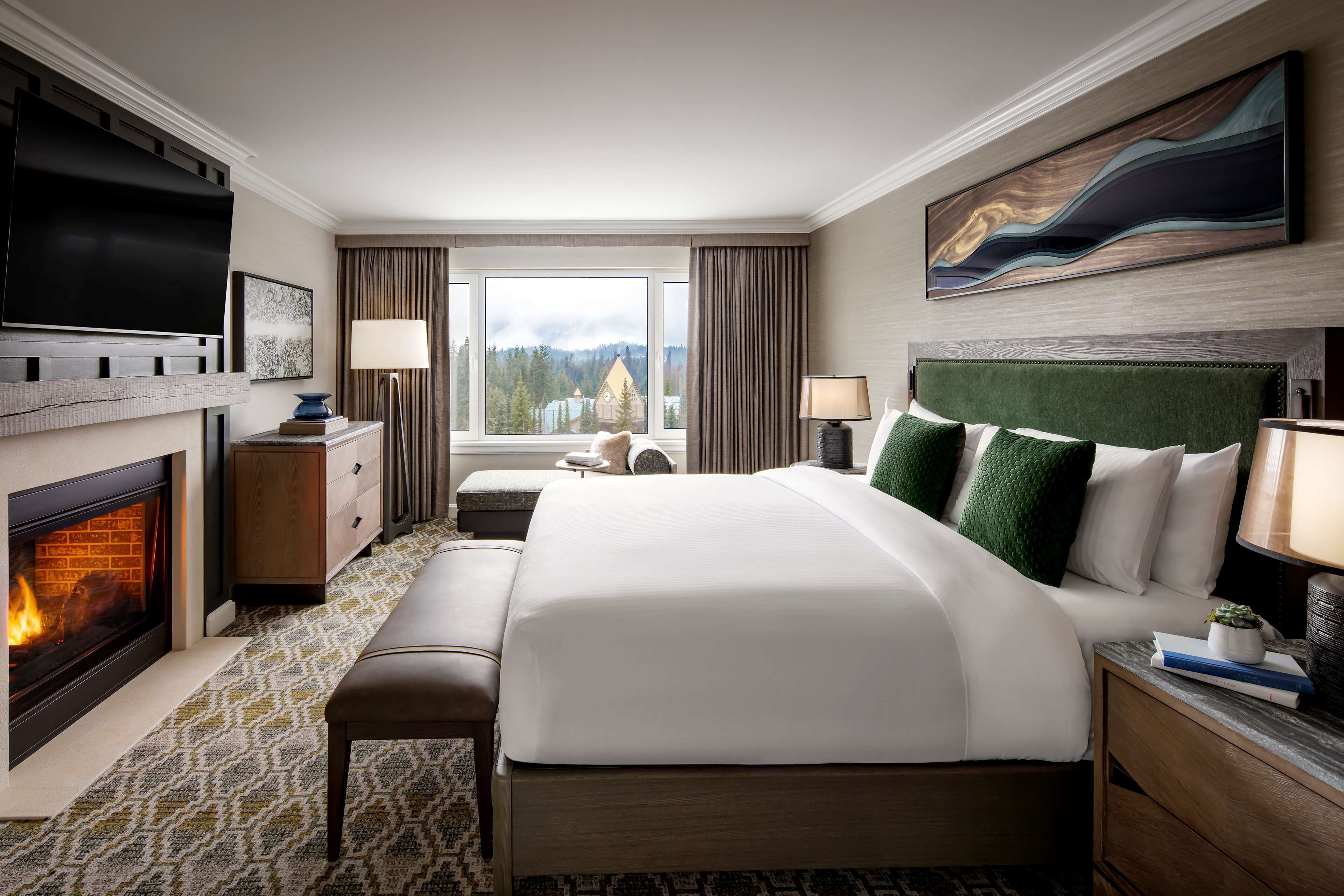 A hotel room with a large bed, a fireplace, a television, and a view of a mountain.