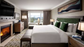 A hotel room with a large bed, a fireplace, a television, and a view of a mountain.