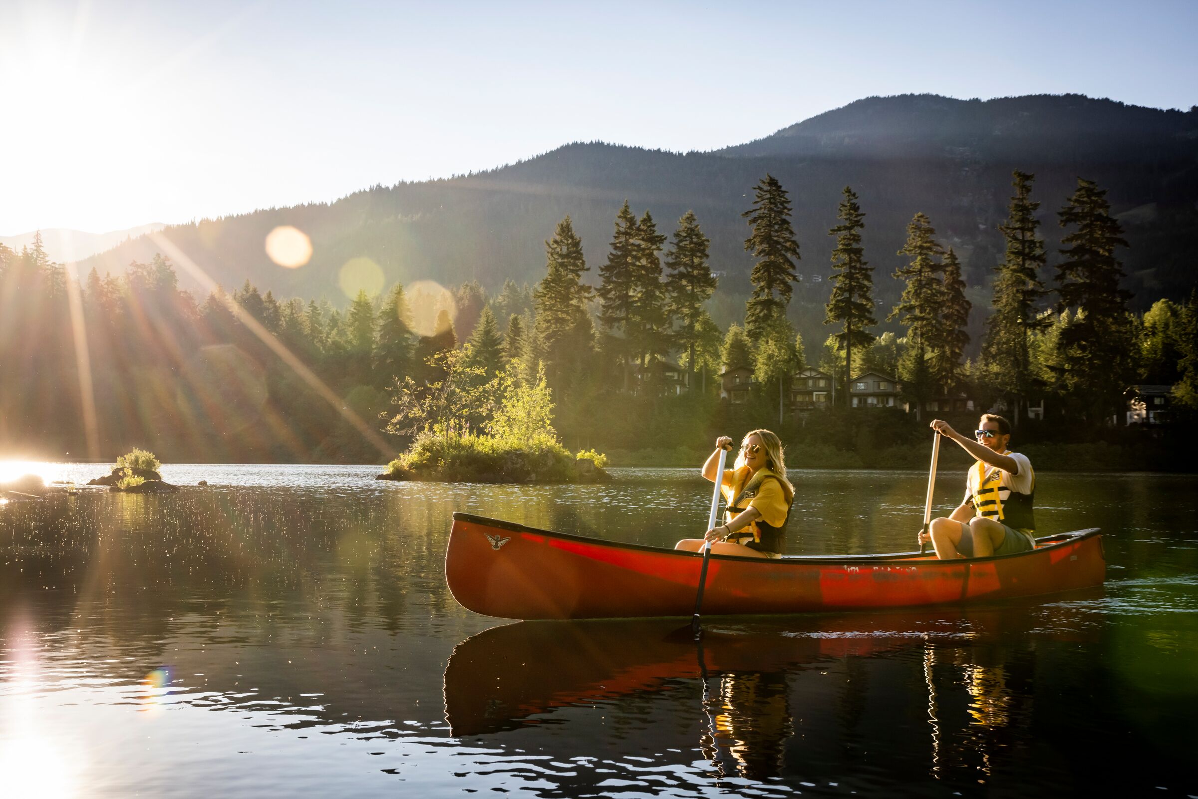 A person in a canoe on a calm lake with mountains in the background.