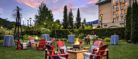 A well-maintained outdoor patio area with red Adirondack chairs, a central fire pit, and tables set up for dining.
