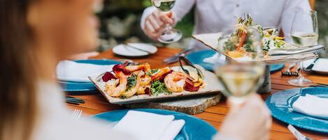 A dining table with plates of food, a wine glass, and a person holding a glass.