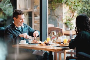 Una pareja cenando en una mesa con alimentos para el desayuno, una jarrón y un vaso de jugo de naranja.