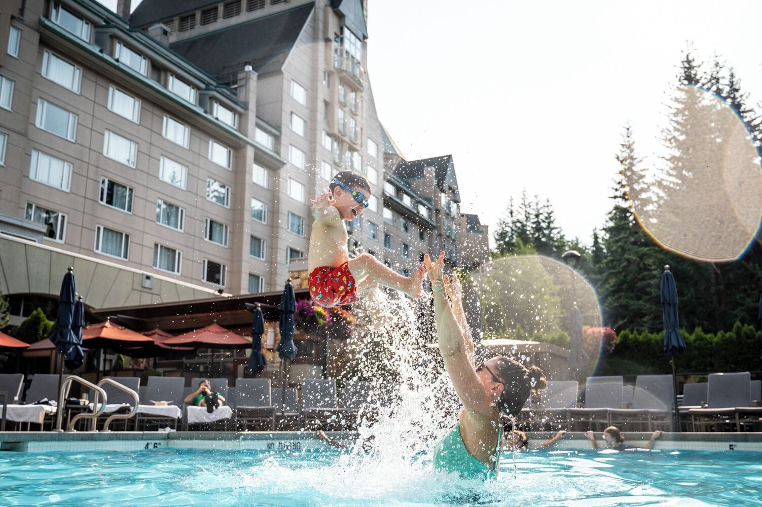 Ein Hotelpoolbereich mit einem großen Gebäude im Hintergrund, Liegestühlen und Sonnenschirmen.