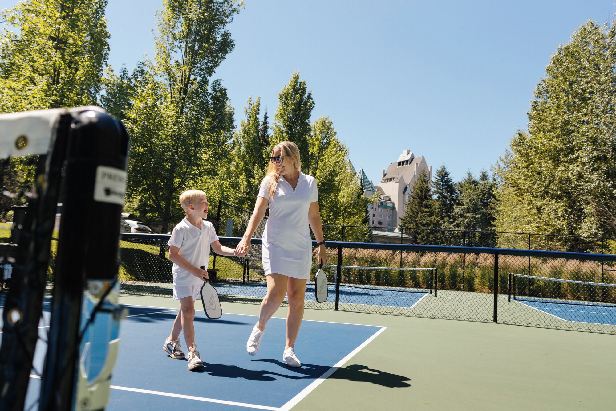 A tennis court with a net, a fence, and trees in the background.