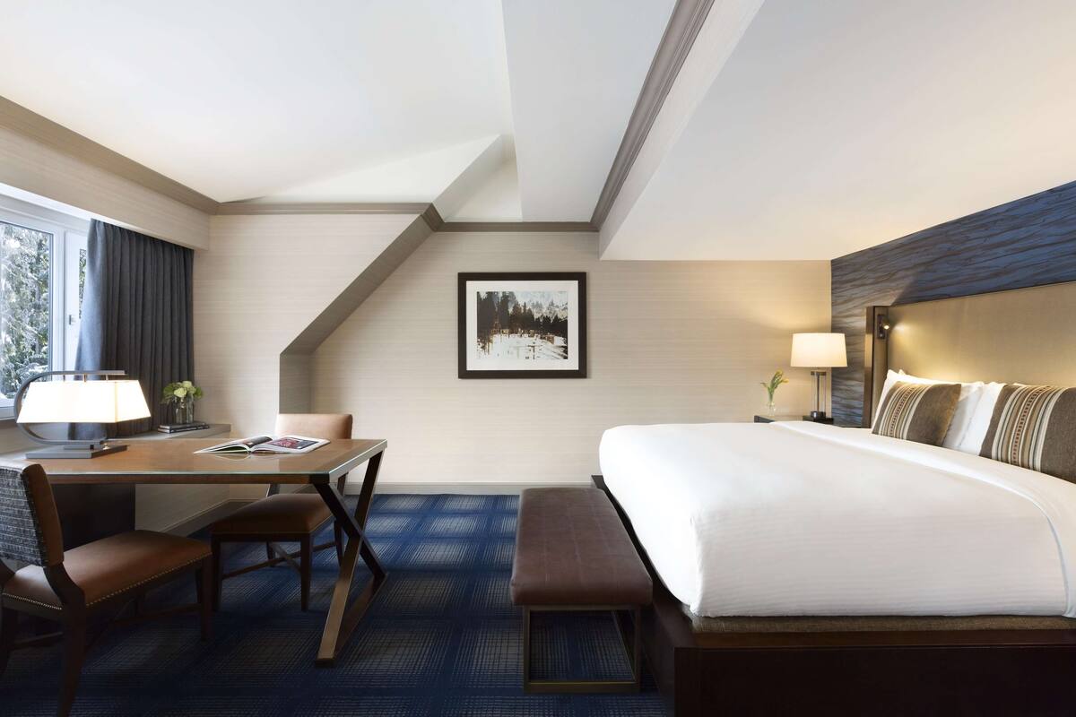Une chambre d’hôtel avec un lit, un bureau, une chaise, une lampe et un tableau encadré au mur.