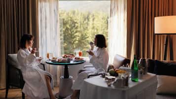 A room with two people seated at a table with breakfast, a lamp, and a view of trees through the window.