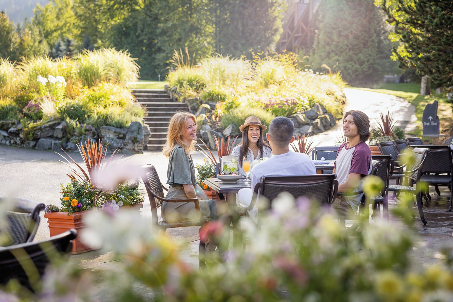 Un groupe de personnes est assis à une table en plein air, avec vue sur un jardin et un escalier en pierre en arrière-plan.