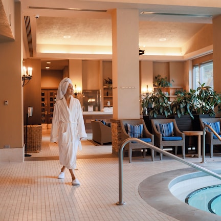 A hotel lobby with a pool, seating area, and a person in a robe walking towards the pool.