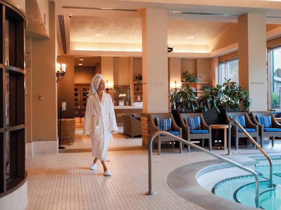 Un hall de hotel con piscina, zona de estar y una persona caminando hacia la piscina con una bata.