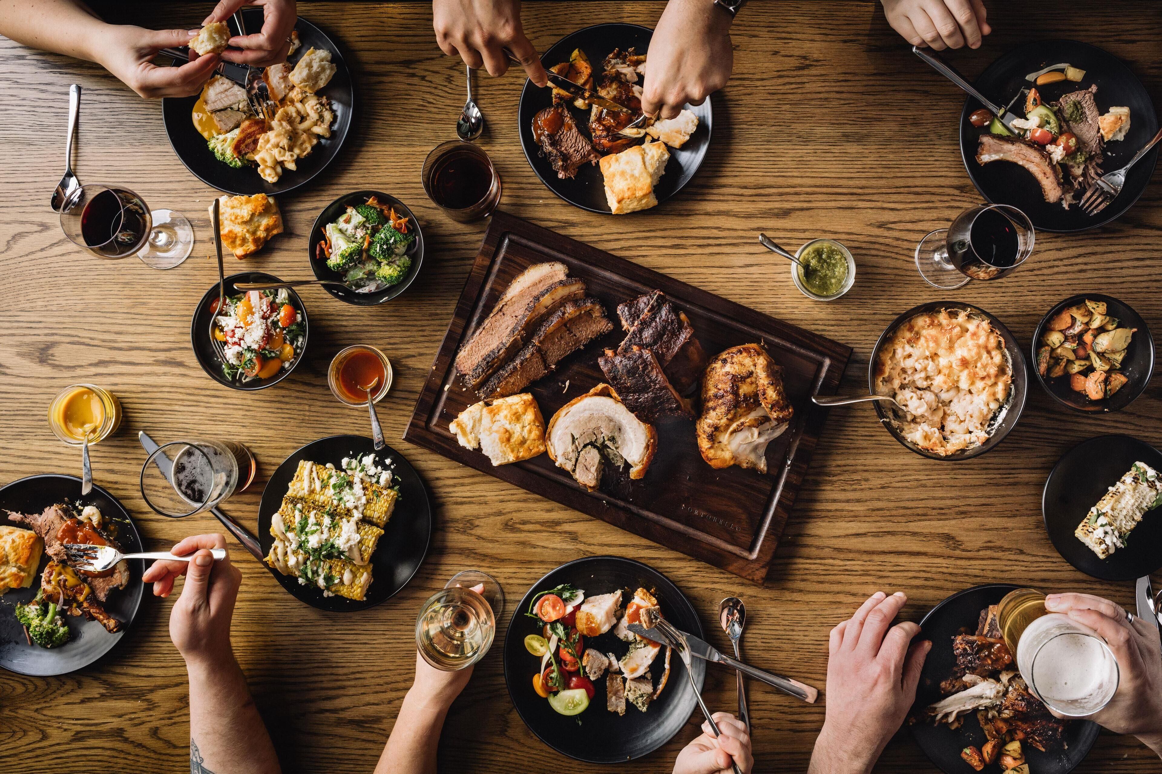 A dining table with various dishes and drinks, surrounded by people eating.