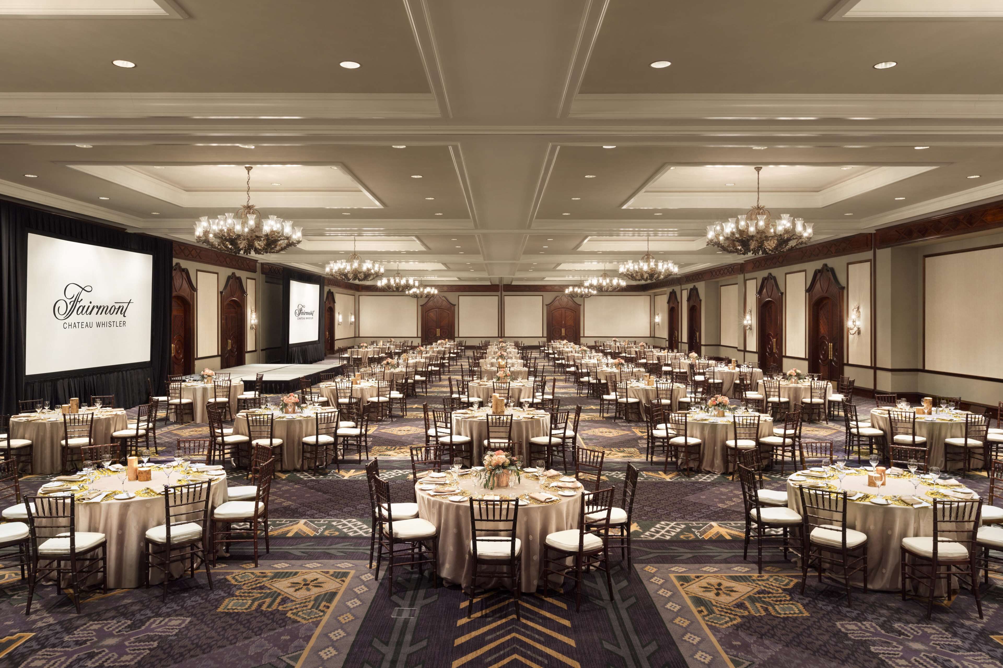 A large banquet hall with round tables, chandeliers, and a projection screen displaying "Fairmont Chateau Whistler".