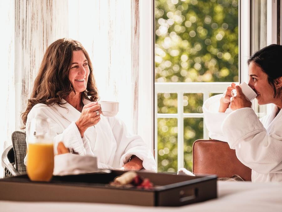 Two individuals in white robes sitting at a breakfast table with a tray of food and a glass of orange juice.