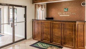 A reception area with a wooden reception desk, a clock, and a sign that reads "Quality Inn by Choice Hotels."