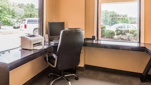 A hotel room with a desk, computer, and chair. There is a window with a view of the street and parked cars.