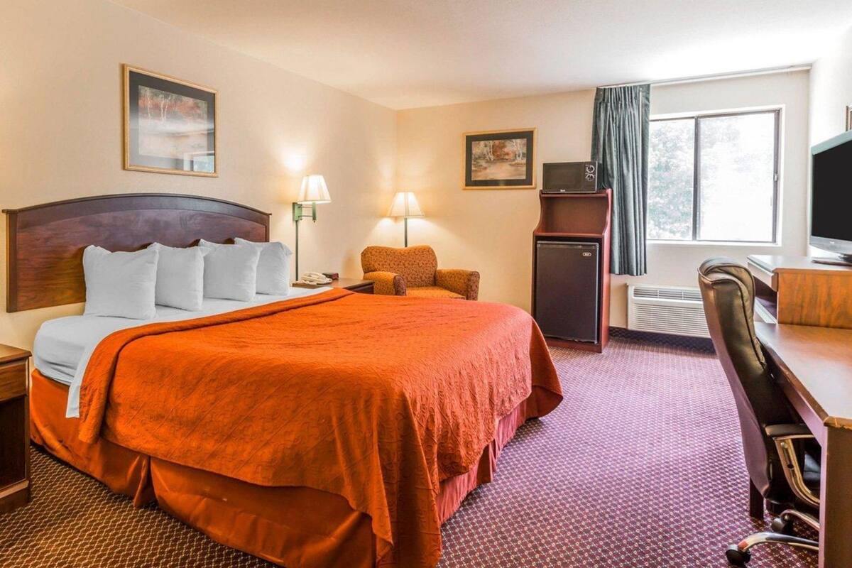 Une chambre d’hôtel équipée d’un lit, d’un bureau, d’une chaise, d’une télévision et d’un petit réfrigérateur.