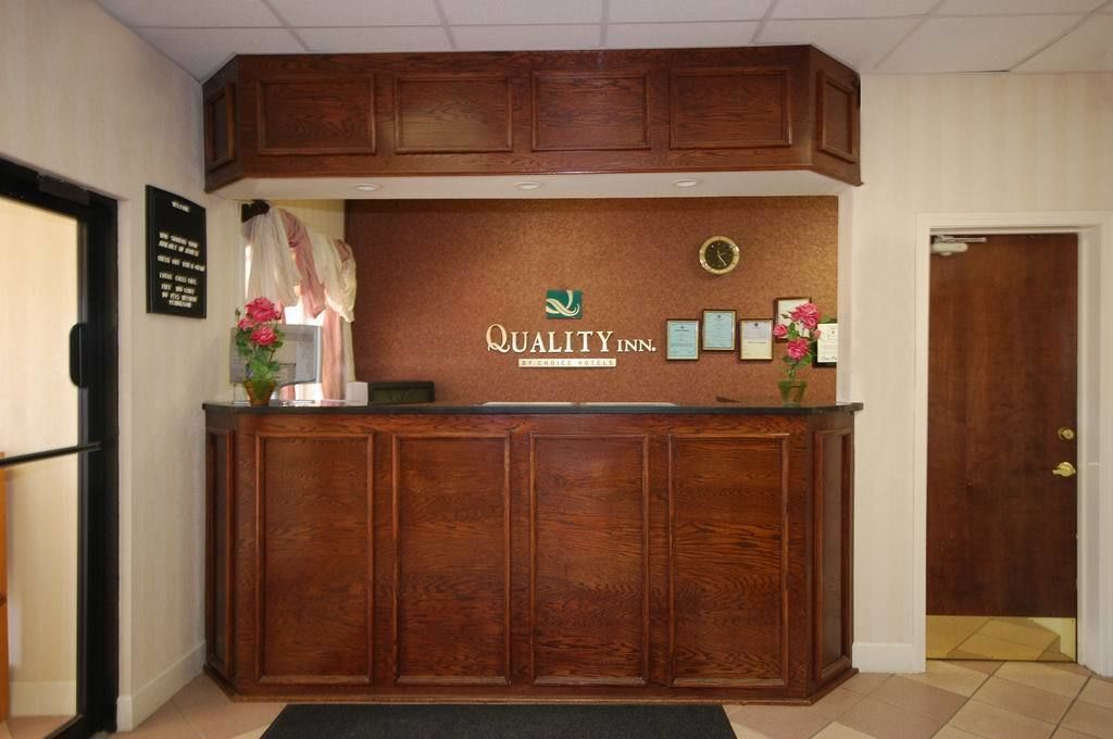 A reception desk with a wooden finish, a clock, framed certificates, and a sign for Quality Inn.