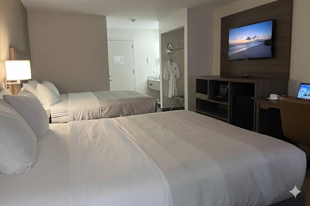 Une chambre d’hôtel avec deux lits, une télévision, un bureau avec un ordinateur et une vue sur la plage.